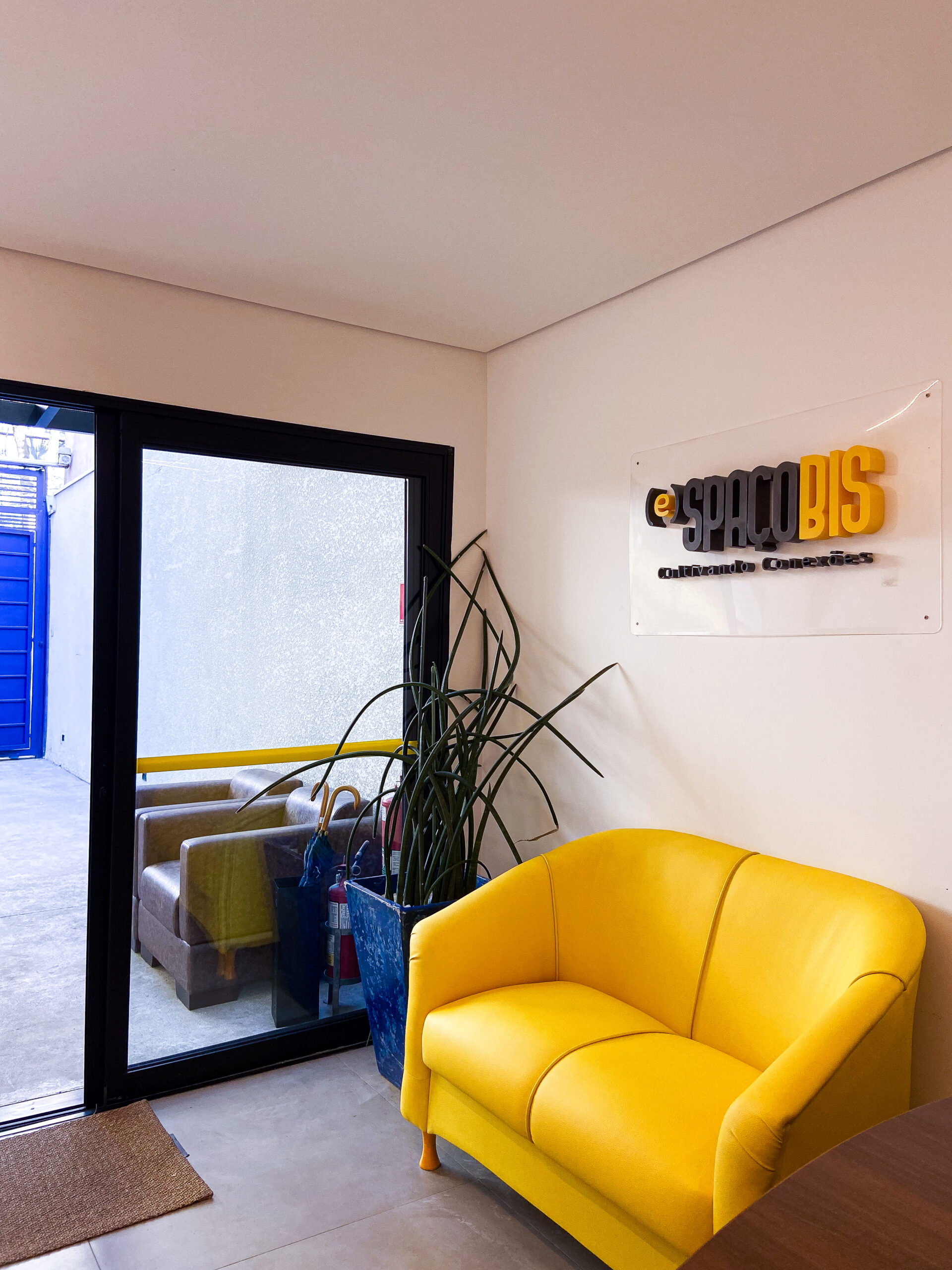Recepção do Espaço BIS com sofá amarelo, logo na parede e luz natural.